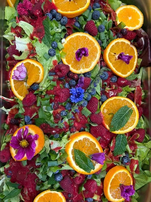 Salatplatte mit Orangenscheiben, Beeren und essbaren Blüten